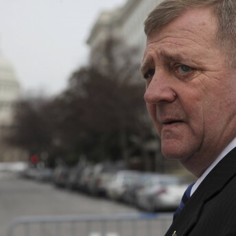 A man in a suit turns his head to the camera. In the background, we can see the US Capitol.