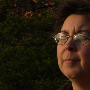 Close-up of a woman's face. She wears golden circled eyeglasses.