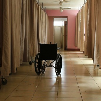 Still of A Quiet Inquisition. Shot of a wheelchair in a hospital room with curtains between each bed.