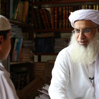 Still from Among The Believers. A man and a child are speaking in a room full of books.