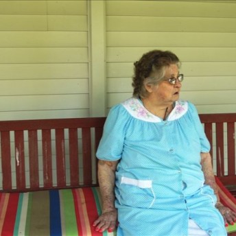 An elderly woman is sitting on a colorful bench.