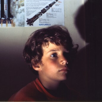 A young boy looks away from the camera. The light illuminates part of his face and leaves the rest in the shadow.