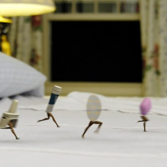 Still from Orgasm Inc. Four tiny medicinal items with human legs run across a bed. There is an open window in the background with floral curtains.