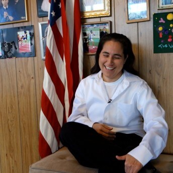 Still from Southwest of Salem. A person sits on a bench and laughs, next to them there is a US flag.