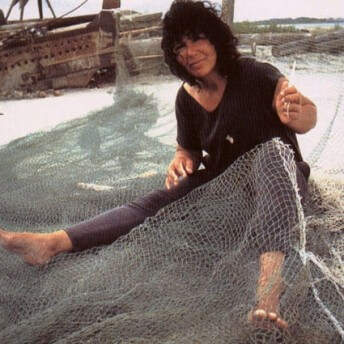 A photo of Diane Wilson sitting on the ground with a fishing net draped over her lap.
