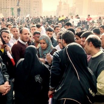 Still from Words of Witness. A large crowd of people gathers outside in a protest. Some hold-up signs.