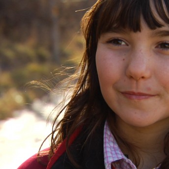 Still of A Place at the Table. Close-up of a girl with medium hair and a fringe. It's daytime and the sunlight reflects on her hair. She is slightly smiling.