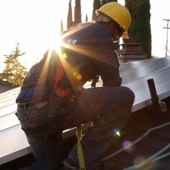 A man is installing solar panels; he wears a helmet, and is stepping down a ladder.