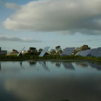 Solar panels at the shore of a lake, surrounded by green vegetation.