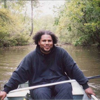 A man wearing a black hoodie and pants is rowing in a boat.