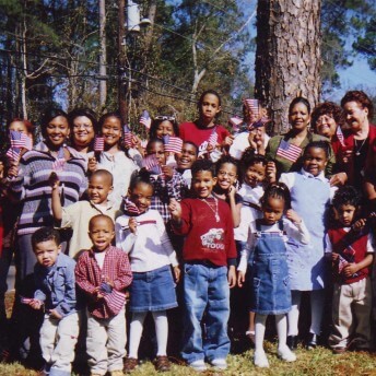 A group of women and children look directly at the camera and hold US flags in their hands.