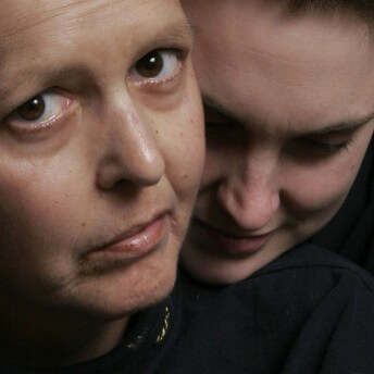 Still from Freeheld. Close up of a woman's face, looking up. Behind her, close up of another woman's face, leaning on her shoulder.