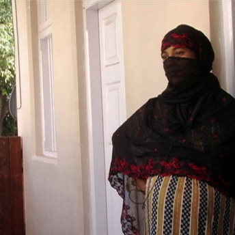 Still from Made in India. A pregnant woman is stading outside. Her hair and the lower half of her face is wrapped in a black and red dupatta.