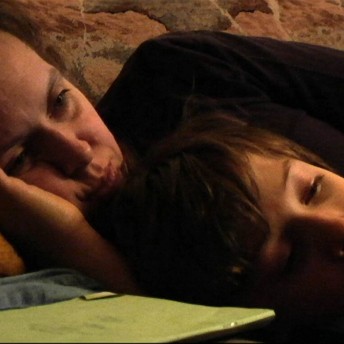 Still from My Perestroika. A woman and a boy lie on their sides on a couch, her right hand is under her face on the pillow.