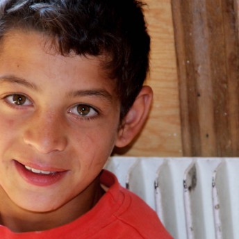 Still from Our School. Close-up of a young boy smiling and wearing a red tshirt.