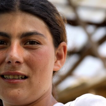 Still from Our School. Close-up, slightly upward angle of a young woman smiling at the camera.