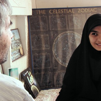 Sepideh is talking to a man that has his back turned to the camera. Behind her, there is a big framed poster that says "The Celestial Zodiac"