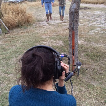 Production still from Hot Girls Wanted. A woman is seen from behind, and she is wearing headphones and holding a camera that is pointed in front of her towards a man and an adolescent girl walking side by side.