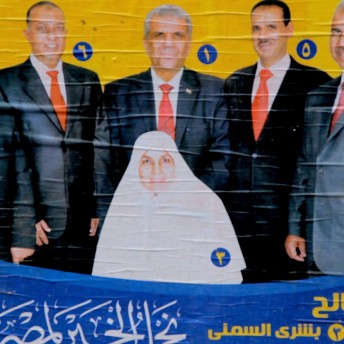 Still from The Vote. Photograph of a poster pasted on a wall. Three persons in suites are behind a person wearing a hijab.