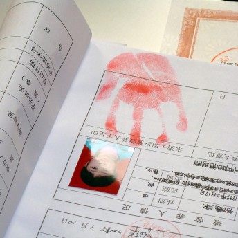 An upside-down Chinese document with a portrait of a young kid affixed to it. A red handprint is on the page. Color photograph.