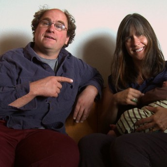 Still from Bag It. A couple is sitting on a couch. The man points at the woman. The woman is feeding a baby in her arms.