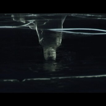 Still from Our City Dreams. The dark reflection of an upsidedown egyptian sculpture on a black surface.