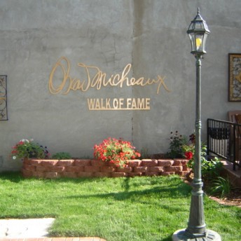 Still from Oscar's Comeback. In a courtyard area, the signature of Oscar Micheaux and words "Wall of Fame" are in a rose gold lettering on a cement wall. There are lamp posts and chairs around as well.
