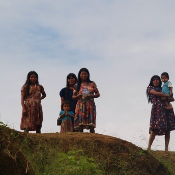 A Group of people looks at the camera standing atop a hill. The background is a cloudy sky. Color photograph.