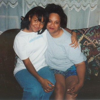 A teenager and a woman sitting on a sofa hug each other while posing in front of the camera.