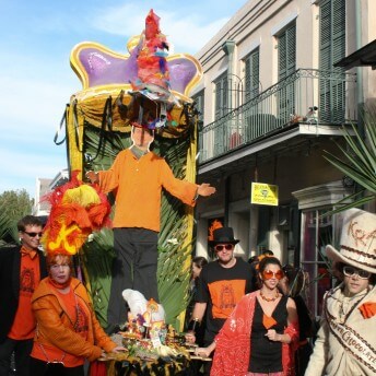 Still from My Louisiana Love. A few people wearing hats carry a parade float down a street.