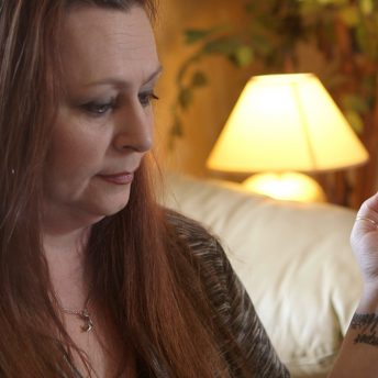 Still from Roll Red Roll. A woman sitting on a couch with a cigarette in her left-hand looks down.