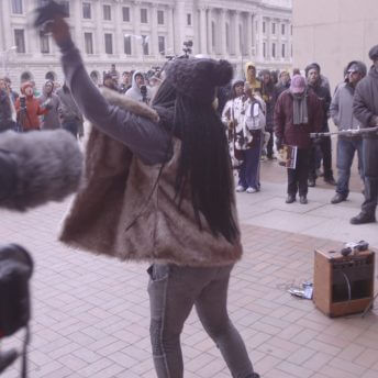 A woman speaking with a microphone in front of people.