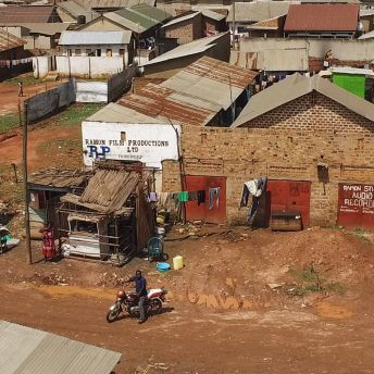 Still from Once Upon a Time in Uganda. An slight bird's eye view of a small village. There are people walking and on bikes.