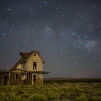 A still from The Guardian of Memory. A house sits off to the side on a grassy plain. It is night time and the sky is filled with stars and hues of blues and purples.