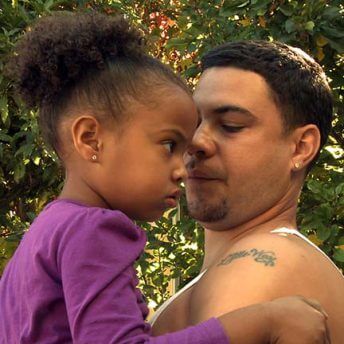 Waymond Hall holding a young kid in front of shrubbery. Color photograph.