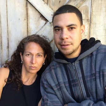 Waymond Hall sitting next to Jane Greenburg in front of a fence looking straight into the camera. Color photograph.