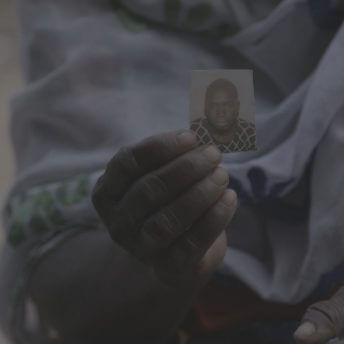 Still from Number 387. A close-up shot of a hand holding a small photograph of a man looking at the camera.