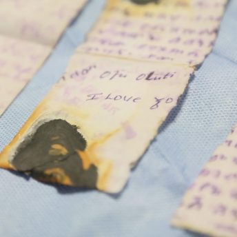 Still from Number 387. A close-up shot of a torn and burned handwritten note placed on blue fabric.