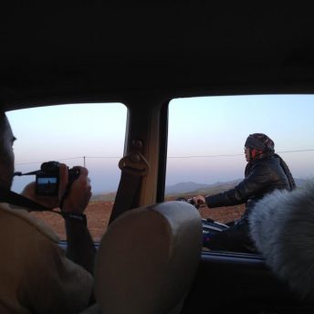 Taken from a moving car, a cameraman records a man on a motorcycle.