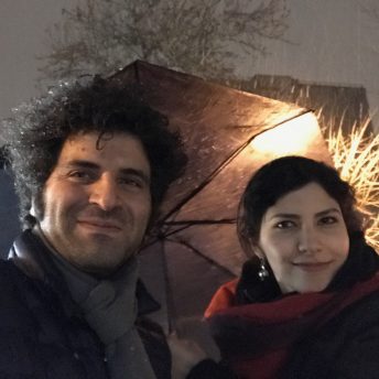 Sara Khaki and Mohammad Reza Eyni look directly at the camera and smile. It's nighttime and they wear winter clothes.