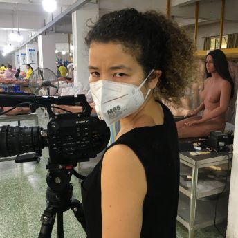 Production still from Ascension. Director Jessica Kingdon is working with a camera in a sex doll fabric and is turning to look at the camera.
