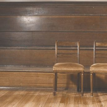 Still from Milisuthando (working title). Two wooden chairs sit infront of wooden stadium style bench seating.