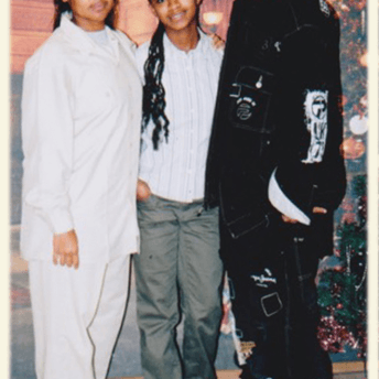 Archive photo of three young people looking at the camera and smiling. They are embracing each other and standing next to a Christmas tree.