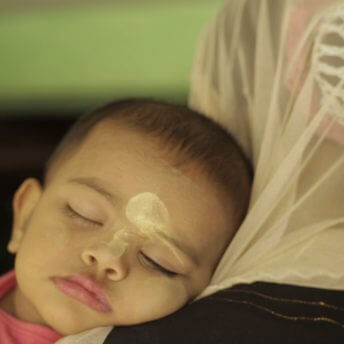 Still from Midwives. A young boy sleeps on the shoulder of a woman wearing a headscarf.