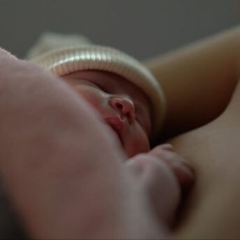 A baby with a white knitted hat sleeping on an unclothed chest, both obscured by an unidentified body part