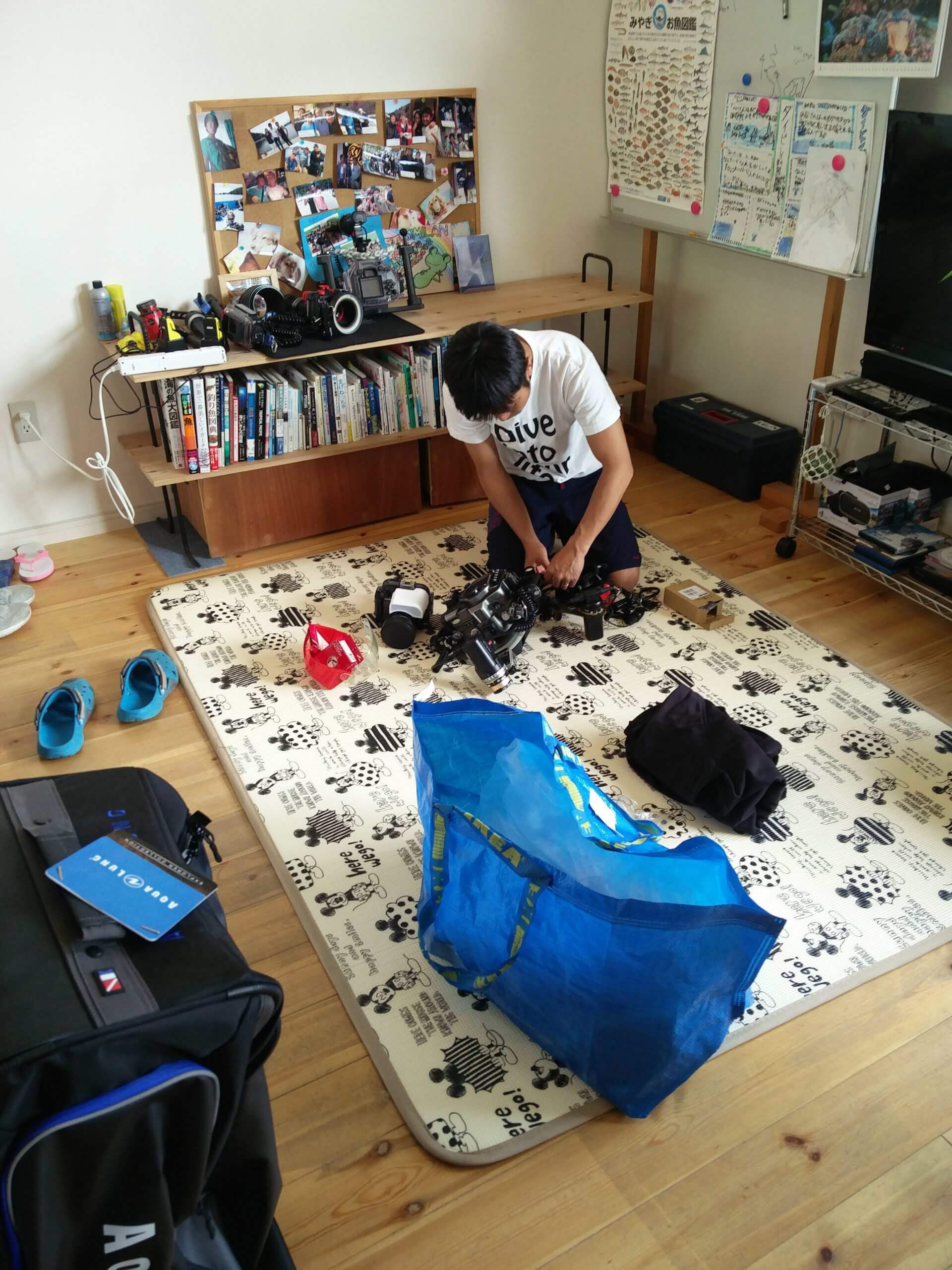 Production still from All of Our Heartbeats Are Connected Through Exploding Stars. A camera person on the floor setting camera equipment ready. They are inside of a living room.