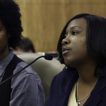Still from Belly of the Beast. Kelli Dillon is testifying in court, in front of a microphone.
