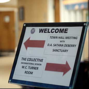 Still from I am not going to change 400 years in four. Photography of a sign with two opposite red arrows. To the left: Townhall meeting with D.A. Satana Deberry, to the right: The collective informational center.