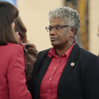 Still from I am not going to change 400 years in four. Two women talking to each other, one wears a red blazer, and the other one has short hair, a red shirt, a black blazer, and glasses.