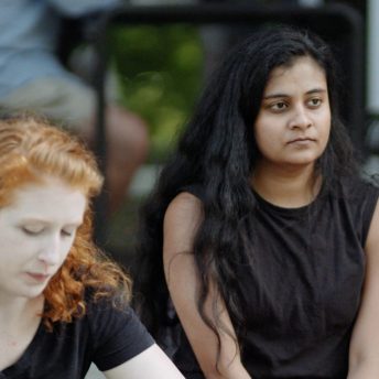 Three women are sitting and looking away from the camera. All of them wear black clothing.